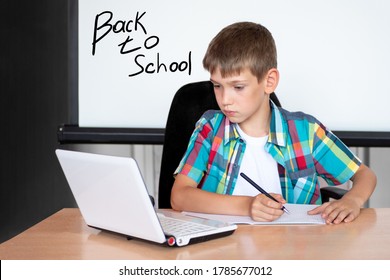 A cute boy is sitting at a table, looking at a laptop, writing homework or preparing for an exam. Concept Back to school