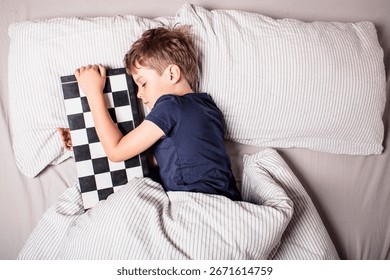 Cute boy sleeping in bed while hugging a chessboard, dreaming about strategy, intelligence and childhood imagination. Concept of passion for chess, learning,peaceful rest. Future chess grandmaster.