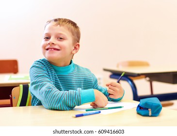 cute boy with special needs writing letters while sitting at the desk in class room