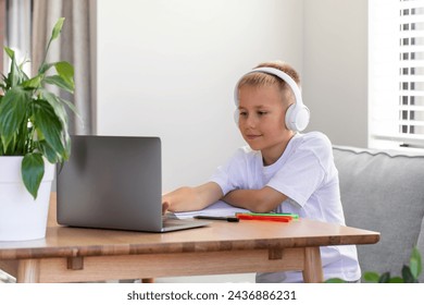 A cute boy is studying at an online school. The boy is sitting in front of a laptop with headphones and listening to the teacher. The concept of education. - Powered by Shutterstock