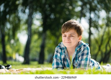 Cute boy in summer park lying on blanket and reading book