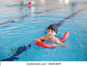 Cute Boy Swimming With A Red Foam Noodle In Indoor Pool
