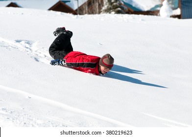 Cute Boy In Tobaggan Riding Down On His Body On A Snow Hill.