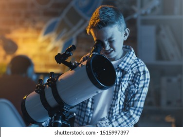 Cute boy watching stars through a telescope at night in his bedroom, imagination and discovery concept
