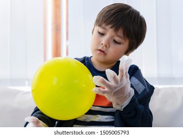 Cute Boy Wearing Disposable Protective Plastic Glove And Holding Yellow Balloon,Kid Preparing Science Project About Static Charged, Child Looking Curiously At Science Experiment,Home Schooling Concept