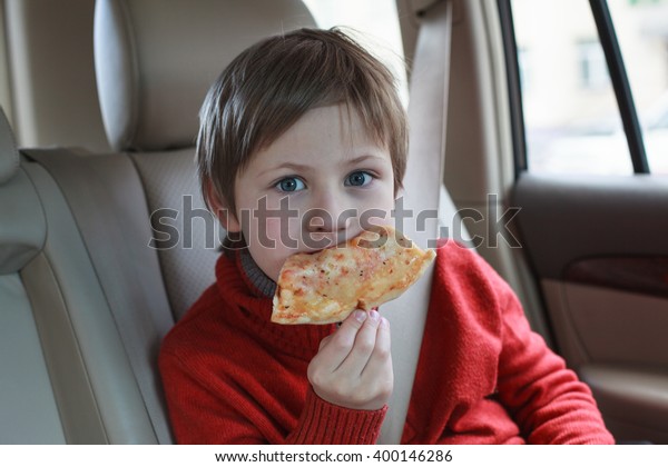 cute boy wearing safety car belt and eating pizza\
margarita in the car