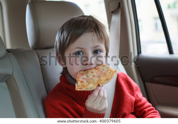 cute boy wearing safety car belt and eating pizza\
margarita in the car