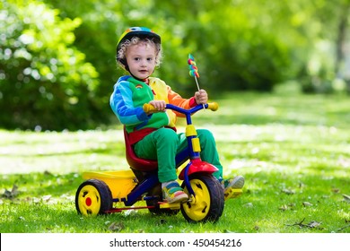 Cute boy wearing safety helmet riding his tricycle in sunny summer park. Kids ride bicycle. First bike for little child. Active toddler kid playing and cycling outdoors. Kids play in the garden. - Powered by Shutterstock