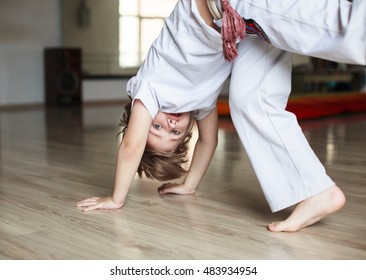 Cute boy in white clothes practicing capoeira (brazilian martial art that combines elements of dance, acrobatics and music)  in gym

