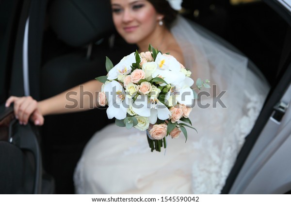 Cute bride with a bouquet in her hand in a car in\
the back seat