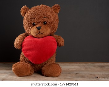 cute brown teddy bear holding a big red heart and sits on a black wooden background, holiday gift for Valentine's Day