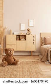 Cute brown teddy bear sitting on the floor of beige bedroom interior with wooden commode