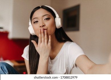 Cute brown-eyed girl in big headphones makes selfie and blows kiss