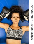 Cute, brunette female boxer smiling at the camera while lying on the floor of the boxing ring