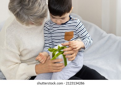 cute brunette hair boy and his grandma are unboxing a gift, sitting on the bed. grey hair granny receives gift from nephew. mother's or woman's day. two different generations.