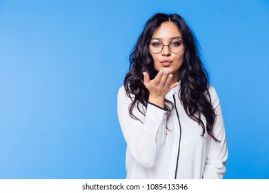 Cute Brunette in white blouse and glasses on blue sending air kiss background