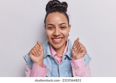 Cute brunette woman jumps exuberantly her fists clenched in celebration with infectious smile poses for camera basking in glory of success smiles toothily wears denim clothes isolated over white wall