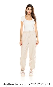 Cute brunette woman in white shirt and loose white trousers posing on a white studio background. Full length, front view.
