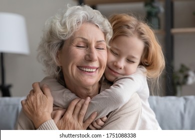 Cute caring small granddaughter embrace cuddle smiling middle-aged 60s grandmother, relax together at home, little grandchild hug senior grandparent, show love and gratitude, family unity concept