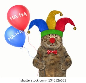 The Cute Cat In A Jester Hat Holds Two Color Balloons. April Fools Day. White Background. Isolated.