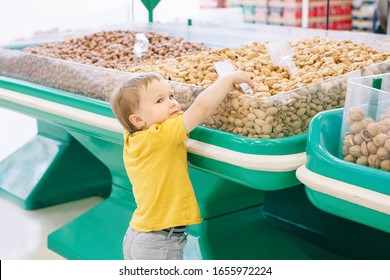 Cute Caucasian Baby Child Choosing Nut In Supermarket. Funny Toddler Boy In Grocery Store Packing Produce. Healthy Tasty Summer Food Snack For Kids. Product Food Allergy Concept.
