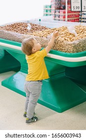 Cute Caucasian Baby Child Choosing Nut In Supermarket. Funny Toddler Boy In Grocery Store Packing Produce. Healthy Tasty Summer Food Snack For Kids. Product Food Allergy Concept.
