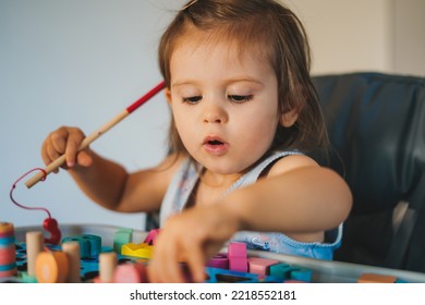 Cute Caucasian Baby Girl Sitting In Baby Chair And Playing With Educational Colorful Toys. Baby Toddler Sits In A High Chair. Happy Healthy Kid Play Alone.