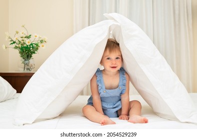 Cute Caucasian Blonde Baby Girl Play,have Fun On White Sheet,blanket Sit Under Soft Pillow House In Bedroom.Adorable Smilng Infant Of 1-2 Year Old On Bed In Modern Interior.Selective Focus