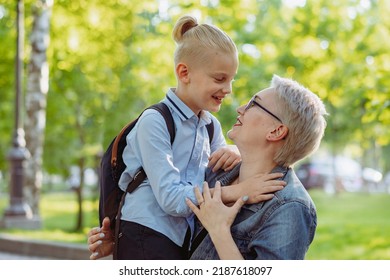 Cute Caucasian Blonde Boy With Ponytail Going To School. Mother Having A Conversation With Child, Saying Goodbye And Hugging. Back To School Concept