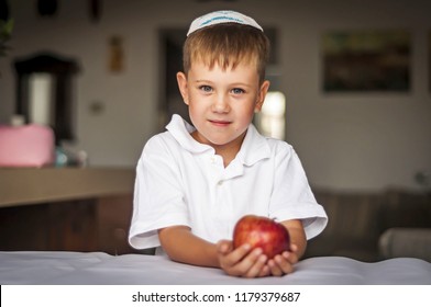 Cute Caucasian blue-eyed boy in a traditional Jewish white kippah cap with an apple in his hands. Russian Jewish boy celebrating Jewish New Year - Rosh Hashanah.