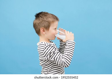 Cute Caucasian Boy Drinks Milk Or Kefir From A Glass Glass On A Blue Background. The Benefits Of Milk And Fermented Milk Products For Children. Copy Space