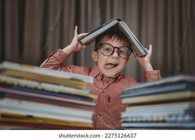 cute caucasian boy wearing glasses making funny face with tongue stuck out covering head with book. Cheerful boy peeking from behind piles of books. Image with selective focus and noise effect - Powered by Shutterstock