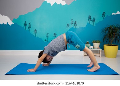 A Cute caucasian child does yoga, downward facing dog position, in a beautiful turquoise  room with mountain mural during coronavirus quarantine. Adho Mukha Svanasana  - Powered by Shutterstock