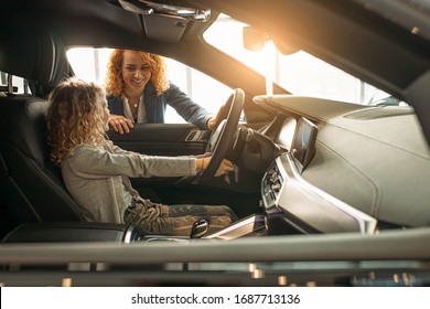 cute caucasian child girl sitting at the wheel of a new buisness class car in dealership. girl's parents going to buy new car, make purchase