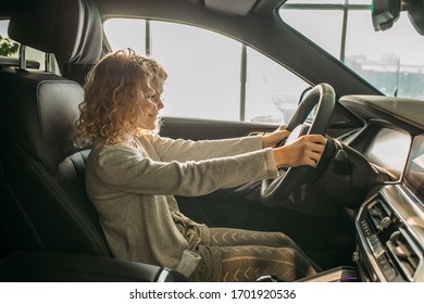 Cute Caucasian Child Girl Sitting At The Wheel Of A New Buisness Class Car In Dealership. Girl's Parents Going To Buy New Car, Make Purchase