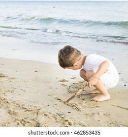 Cute Caucasian Child In White Clothes Writing On The Sand
