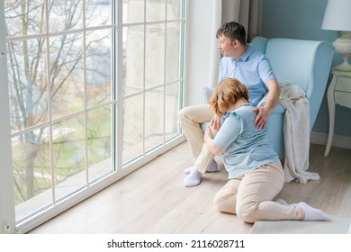 Cute Caucasian Couple Relaxing At Home Man Sits In An Armchair And Woman On Floor Next To Him By A Large Window. Enjoy Serene Happiness In A Bright Bedroom In Casual Clothes