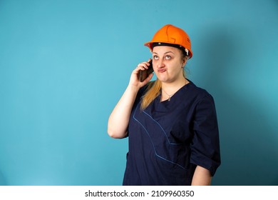 Cute Caucasian Female Construction Worker With Safety Helmet On Head And Phone In Hand. Engineer In Orange Helmet Isolated On Background. Construction Worker Concept .