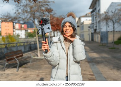 Cute caucasian female vlogger streaming online using mobile phone in the city during a sunny day of autumn - Powered by Shutterstock