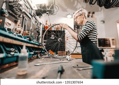 Cute Caucasian female worker holding and repairing bicycle wheel while standing in bicycle workshop. - Powered by Shutterstock