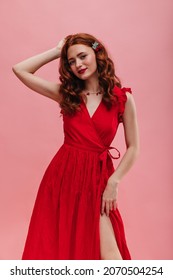 Cute Caucasian Girl With Dark Red Curly Hair In Closed Pink Space. Lady In Bright Red Long Dress With Same Colored Lips Poses, Exposing Her Leg. Beauty, People Emotions And Summer Vacation Concept.