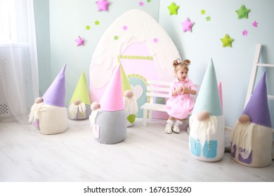 Cute Caucasian Girl With Ponytails Having Fun In A Crowd Of Large Toy Gnomes In Her Bright Room