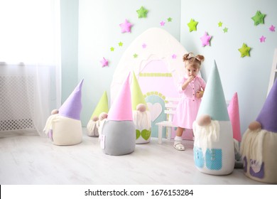 Cute Caucasian Girl With Ponytails Having Fun In A Crowd Of Large Toy Gnomes In Her Bright Room