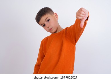 Cute Caucasian Kid Boy Wearing Knitted Sweater Against White Wall Feeling Angry, Annoyed, Disappointed Or Displeased, Showing Thumbs Down With A Serious Look