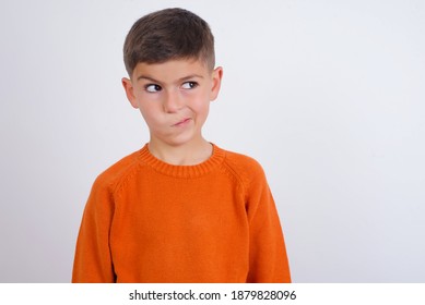 Cute Caucasian kid boy wearing knitted sweater against white wall making grimace and crazy face, screaming out of control, funny lunatic expressing freedom and wild.