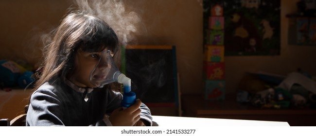 Cute Caucasian Little Girl Alone In Dusty Room With Mask Breathes Through An Inhaler. Home Inhalation Procedure. The Child Is Receiving Respiratory Therapy With Nebulizer