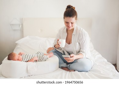 Cute caucasian mom with a newborn baby. Mother with phone and coffee while baby is sleeping, concept of motherhood, social networks and communication of mom in decree - Shutterstock ID 1964750656