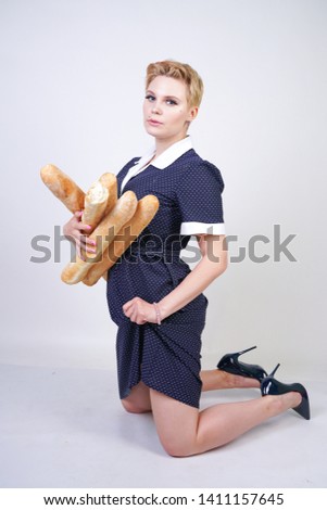 cute caucasian pinup girl wearing vintage polka dot dress and holding baguettes on a white background in the Studio