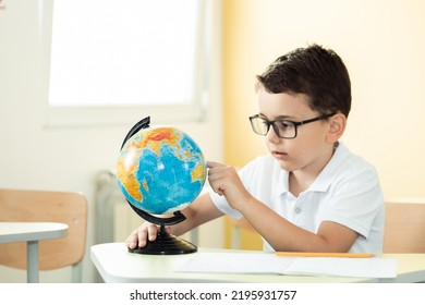 Cute caucasian schoolboy wearing glasses and sits at a desk in the classroom at elementary school. Little boy next the Globe at school. Back to school concept - Powered by Shutterstock