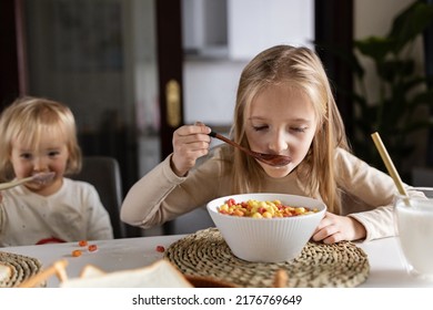 Cute Caucasian Siblings Sitting At Table On Kitchen Early Morning And Preparing Breakfast With Colorful Cornflakes And Milk. Kids Enjoying Life With Healthful Food, Healthy Lifestyle Concept